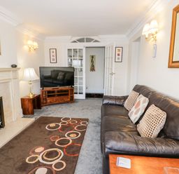 A living room with a black leather sofa a fireplace a television on a wooden stand and a patterned rug at 11 Glyn Garth Mews in Llandegfan near Beaumaris
