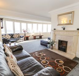 A living room with leather sofas a fireplace a rug with circular patterns and large windows at 11 Glyn Garth Mews in Llandegfan near Beaumaris