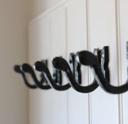 Black metal wall hooks attached to a white wooden panel