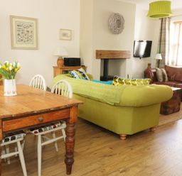 A living room with a wooden dining table and chairs a green sofa a brown leather sofa a wall-mounted TV and a fireplace at Llwyn Onn in Dolwyddelan