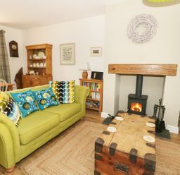 A living room with a green sofa and wooden chest coffee table near a wood burning stove at Llwyn Onn in Dolwyddelan
