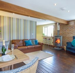 A living room with a brown leather sofa a blue armchair a wood burning stove and a dining table with champagne at Blue Oyster in Mullion near Lizard Point