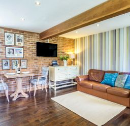 A living room with a leather sofa next to a striped wall and a small dining table with two chairs near a brick wall at Blue Oyster in Mullion near Lizard Point