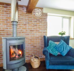 A room with a wood burning stove on a brick wall and a blue armchair with cushions at Blue Oyster in Mullion near Lizard Point