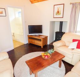 A living room with beige sofas a wooden coffee table with fruit a flat screen tv and a wood stove at The Packing House in Hanley Castle near Malvern