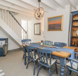 A dining room with a wooden table and blue chairs under a staircase at Marsh Villa in Silloth
