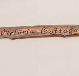 A wooden sign with Victoria Cottage written on it mounted on a white wall at Victoria Cottage in Norham
