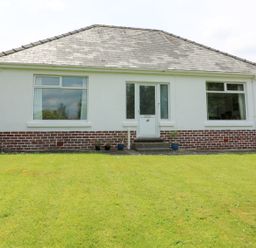 A white bungalow with two large windows and a central door with steps leading to a lawn at White Thorns in Haverfordwest