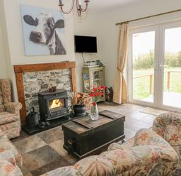 A living room with floral upholstered chairs a stone fireplace a wood stove a wooden chest and glass doors with curtains at Shandrum Brook in Charleville