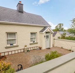 The exterior of a cream colored house with two windows and a door in a fenced yard at Shandrum Brook in Charleville