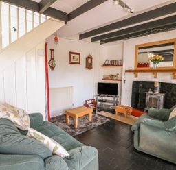 A living room with green sofas a wooden coffee table a fireplace with a mirror above and a tv under wooden stairs at Taliharris Cottage in Llandysul