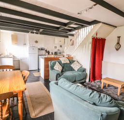 A living area with two sofas a wooden table and chairs a small wooden coffee table a kitchen with appliances and a staircase with a red curtain at Taliharris Cottage in Llandysul