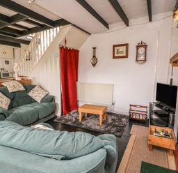 A living room with two sofas a small wooden coffee table a television and a staircase with a red curtain at Taliharris Cottage in Llandysul