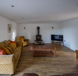 A living room with sofas and armchairs a wooden coffee table a wood stove and a television at Sgubor in Pentraeth