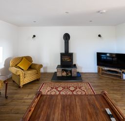 A living room with armchairs a wood stove a television and a wooden coffee table at Sgubor in Pentraeth