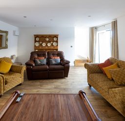 A living room with two brown sofas a wooden coffee table and a wooden shelf with decorative plates at Sgubor in Pentraeth
