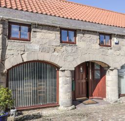 Stone building with arched windows and doors a cobblestone courtyard a blue potted plant and a bench at The Mistal in Glanton near Alnwick