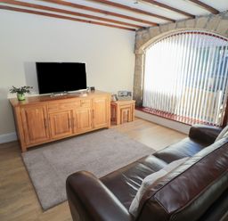 A living room with leather sofas a wooden TV cabinet a television and a large arched window with vertical blinds at The Mistal in Glanton near Alnwick