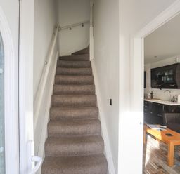 A carpeted staircase leading upstairs with a view into a kitchen and living area with a sofa and wooden coffee table at The Old Post Office 23 High Street in Cemaes Bay