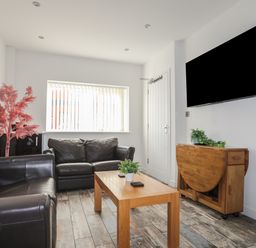 A living room with two black leather sofas a wooden coffee table a wall-mounted tv and a wooden cabinet with plants at The Old Post Office 23 High Street in Cemaes Bay