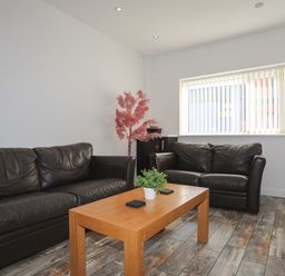 A living room with two black leather sofas a wooden coffee table with a plant and coasters and a window with vertical blinds at The Old Post Office 23 High Street in Cemaes Bay