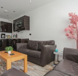 A living area with brown leather sofas a wooden coffee table with a plant and a kitchen with dark cabinets at The Old Post Office 23 High Street in Cemaes Bay