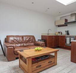 A kitchen and living area with a brown leather sofa a wooden coffee table with green apples and wooden cabinets at The Studio @ The Old Post Office in Cemaes Bay