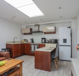 A kitchen with wooden cabinets a refrigerator a brown leather sofa and a wooden coffee table with green apples at The Studio @ The Old Post Office in Cemaes Bay