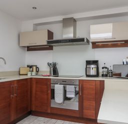 A kitchen with wooden lower cabinets beige upper cabinets a stainless steel oven stove and hood a toaster kettle coffee machine microwave and a sink at The Studio @ The Old Post Office in Cemaes Bay