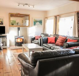A living room with black leather sofas red cushions a white coffee table a fireplace and a television at Beulah Cottage in Green Bottom near Littledean