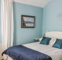 A bedroom with a white bed frame blue pillows blue blanket and a painting on the wall at Beulah Cottage in Green Bottom near Littledean