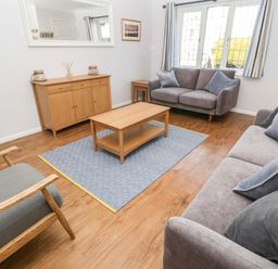 A living room with two gray sofas a wooden coffee table a cabinet and a window at Rockpool in Harlyn Bay near St Merryn