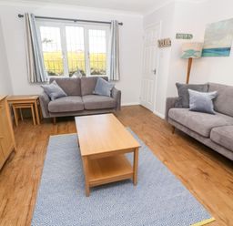 A living room with two gray sofas a wooden coffee table a patterned rug and a sideboard at Rockpool in Harlyn Bay near St Merryn