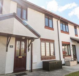 Exterior view of a white two story house with brown doors and windows with a covered porch and outdoor storage boxes at Rockpool in Harlyn Bay near St Merryn