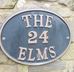 An oval house sign with the text The 24 Elms mounted on a stone wall at The Elms in Milford Haven