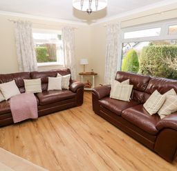 A living room with two brown leather sofas and cushions by windows with curtains at The Elms in Milford Haven