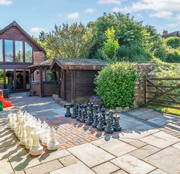 An outdoor patio area with a large chess set a wooden shed a children's play slide and a two-story stone house at The Linhay in Washford near Watchet