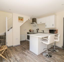 A kitchen with a white island and bar stools next to stairs with striped carpet at Squirrels Drey in Little Dunham near Litcham