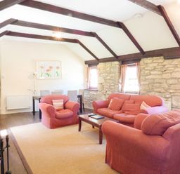 A living room with red sofas a wooden coffee table stone walls and exposed ceiling beams at Parlour Cottage in Marazion