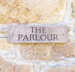 A wooden sign with the words THE PARLOUR on a stone wall at Parlour Cottage in Marazion