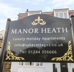 A black signboard with gold decorations displaying information about Manor Heath luxury holiday apartments in Scarborough