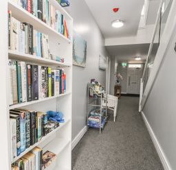 A hallway with a white bookshelf filled with books and a small metal rack with magazines and board games at Manor Heath Apartment 4 Scarborough