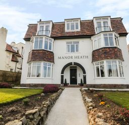 A pathway leading to the entrance of a three-story house with bay windows and a tiled roof at Manor Heath Apartment 4 in Scarborough