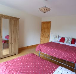 A bedroom with two beds with red polka dot bedding a wooden wardrobe with a mirror and a wooden door at The Slate House in Cahersiveen County Kerry