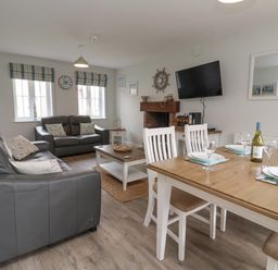 A living room with gray sofas a wooden coffee table a fireplace wall-mounted TV and a dining table with chairs at Flip Flops The Bay near Filey