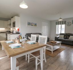 An open plan kitchen and living area with a wooden dining table set with plates and wine glasses two grey sofas and a coffee table at Flip Flops The Bay near Filey