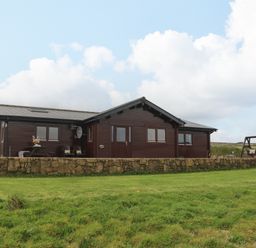 A single story wooden house with a stone wall in front and a swing on the right at Chywolow Lodge in Penzance