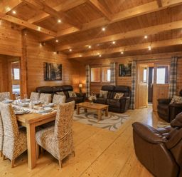 A wooden lodge living room with a dining table set with plates and glasses and leather sofas and armchairs at Chywolow Lodge in Penzance
