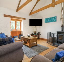 A living room with two sofas blue cushions a wooden coffee table a rug a wood-burning stove and a wall-mounted TV at Mill in Nancegollan nr Porthleven