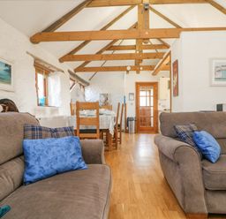 A living room with two sofas and blue pillows a dining table with chairs wooden beams on the ceiling and pictures on the walls at Mill in Nancegollan nr Porthleven